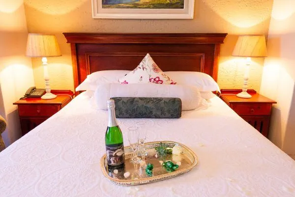 A bed with a tray of wine glasses and chocolates on it