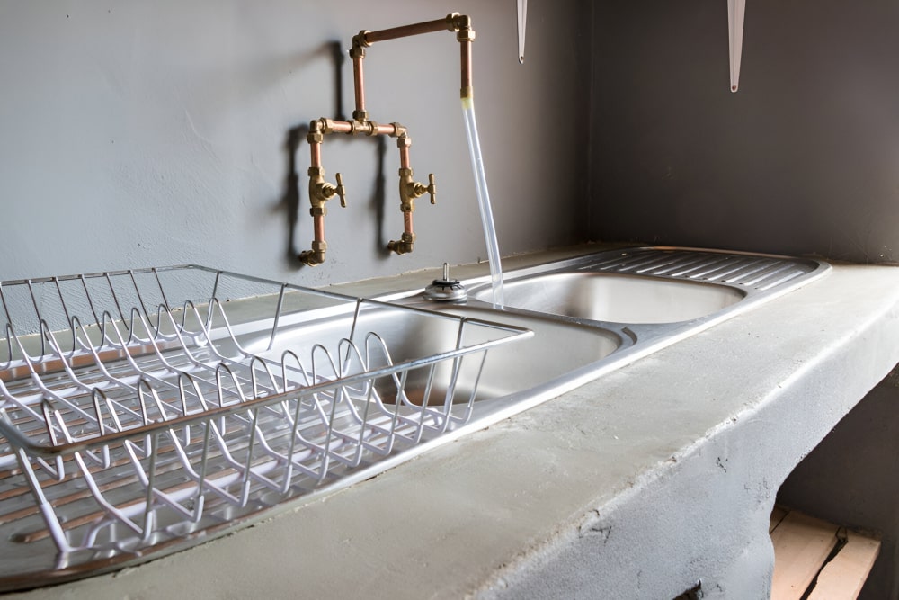 Industrial sink with metal drying racks and exposed plumbing in a kitchen.