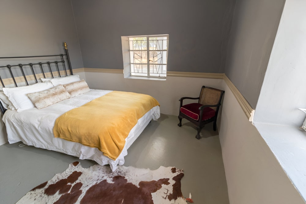 Bedroom with a bed, chair, and cowhide rug on a tiled floor.