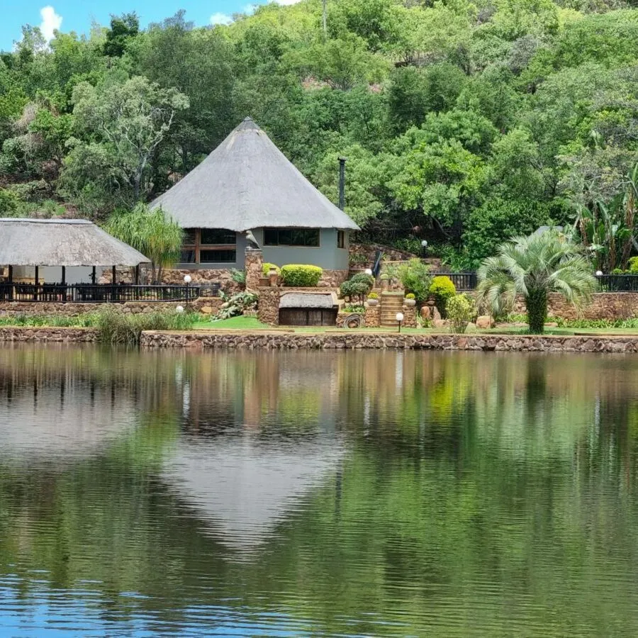 Thatchedroof huts by a lake with lush green trees in the background
