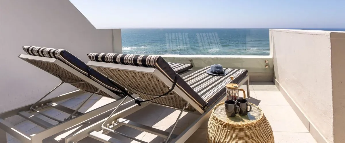 Two lounge chairs on a balcony overlooking the ocean with a small table