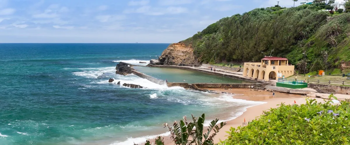 Rocky coastline with a sandy beach green vegetation and a yellow building