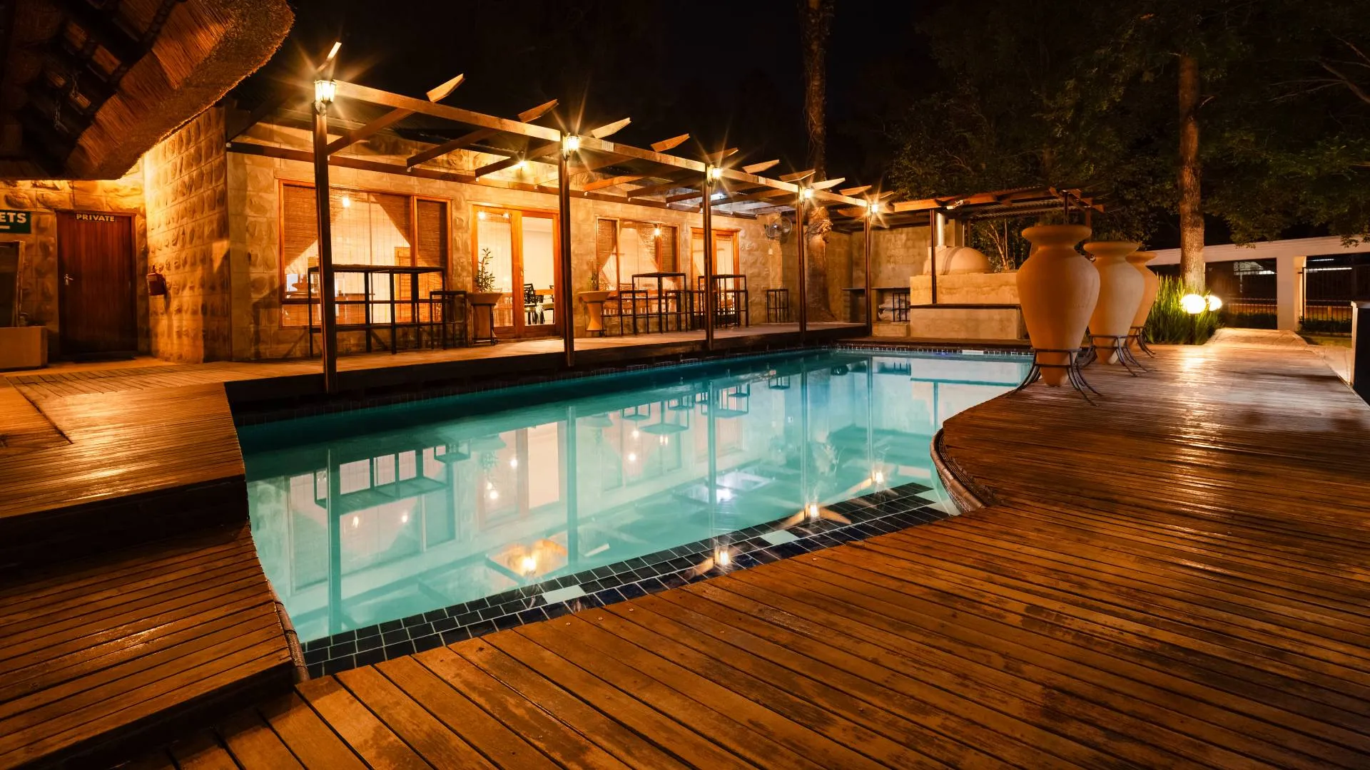 Night view of a poolside area with wooden deck and lit building