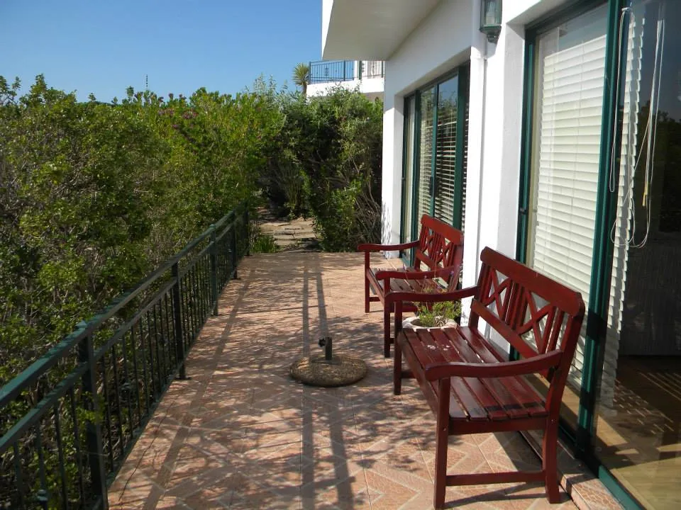 Two red benches on a tiled patio with greenery and a house in the background