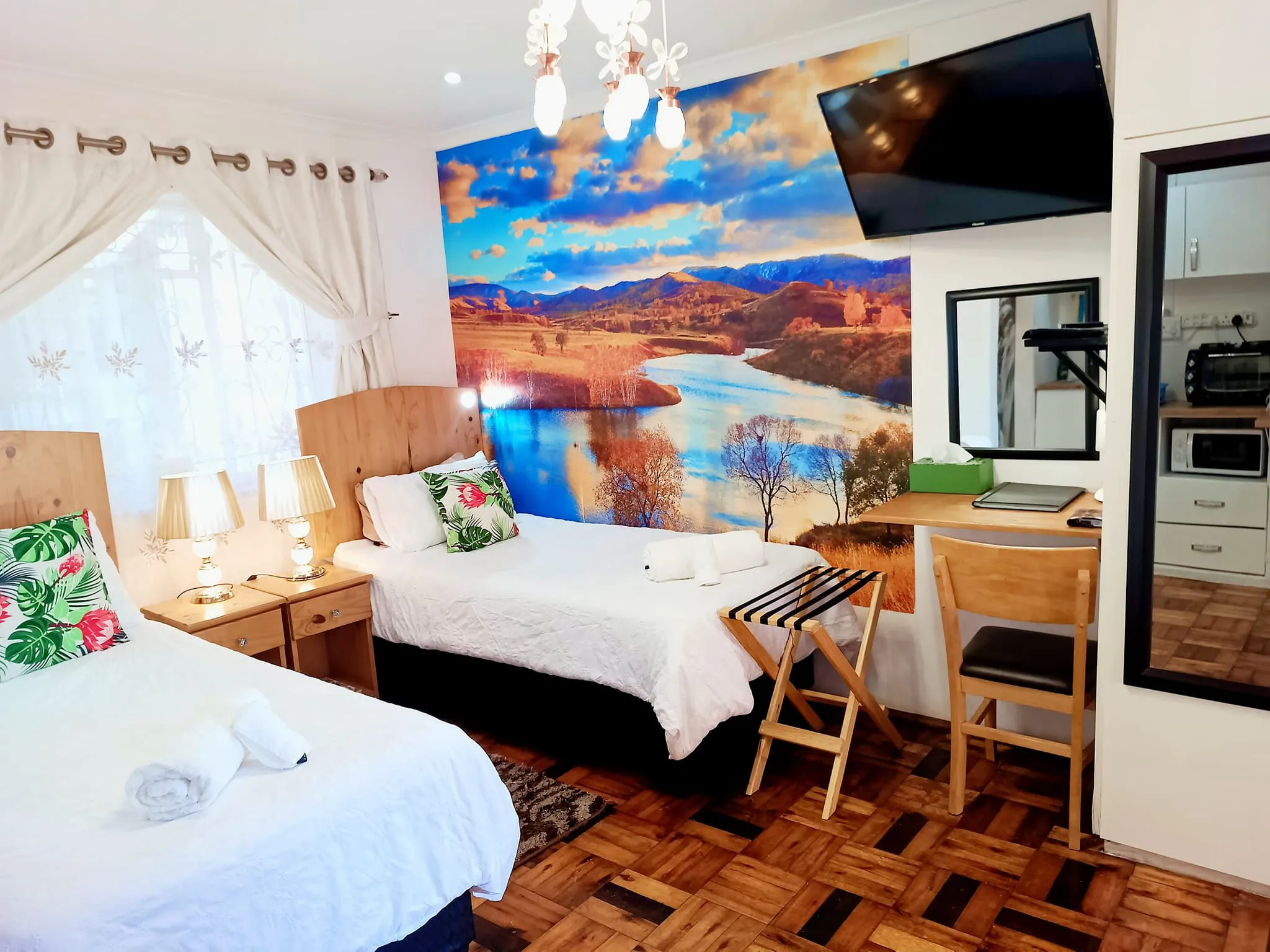 Cozy bedroom with two beds a desk and a scenic mural on the wall