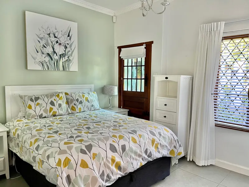 Bright bedroom with patterned bed white furniture and window with white curtains