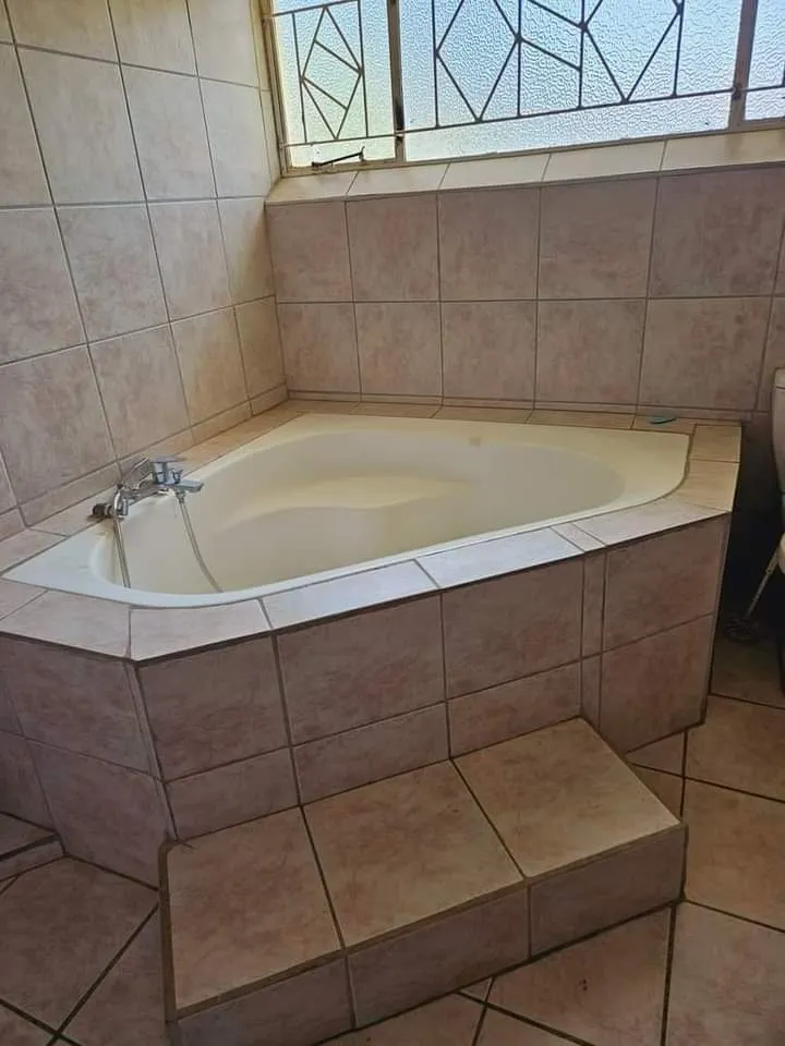 Corner bathtub with tiled steps in a tiled bathroom with a window