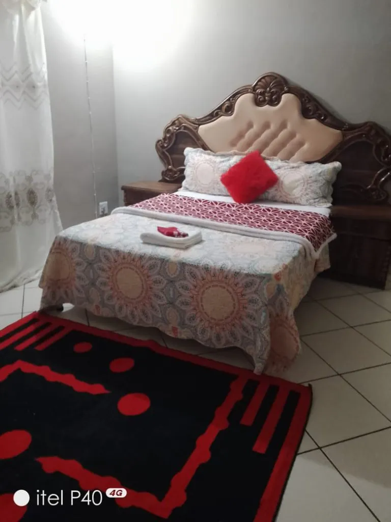 Wooden bed with patterned bedspread and red pillow in a tiled room