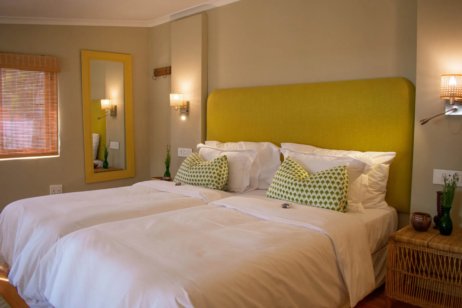 Twin beds with yellow headboard green pillows and bedside tables in a bedroom