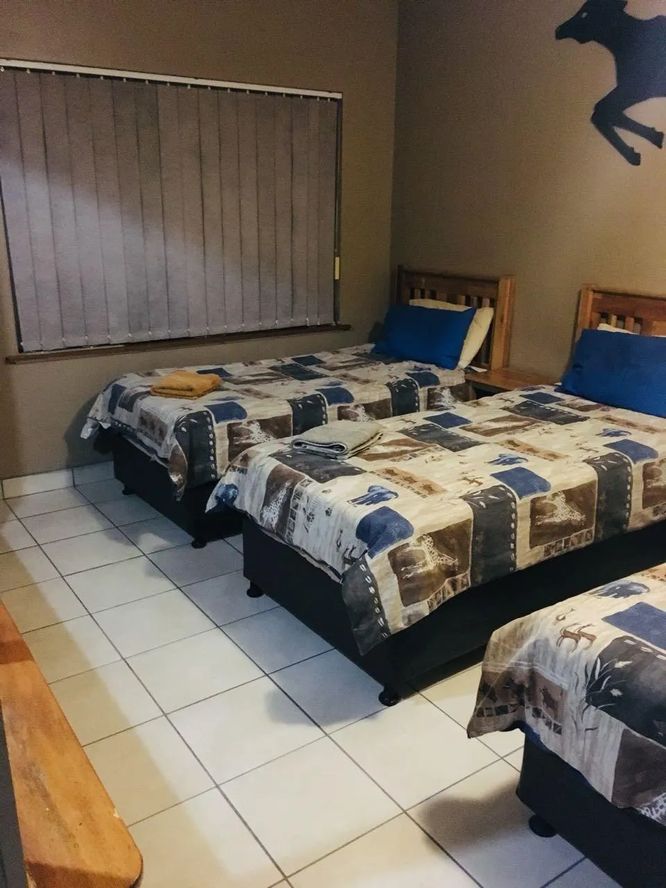 Three beds in a tiled room with wooden headboards and checkered bedspreads