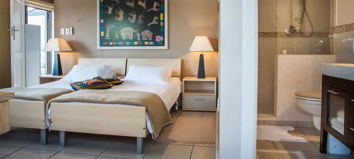 Bedroom with two beds artwork and an adjacent bathroom with a shower and sink
