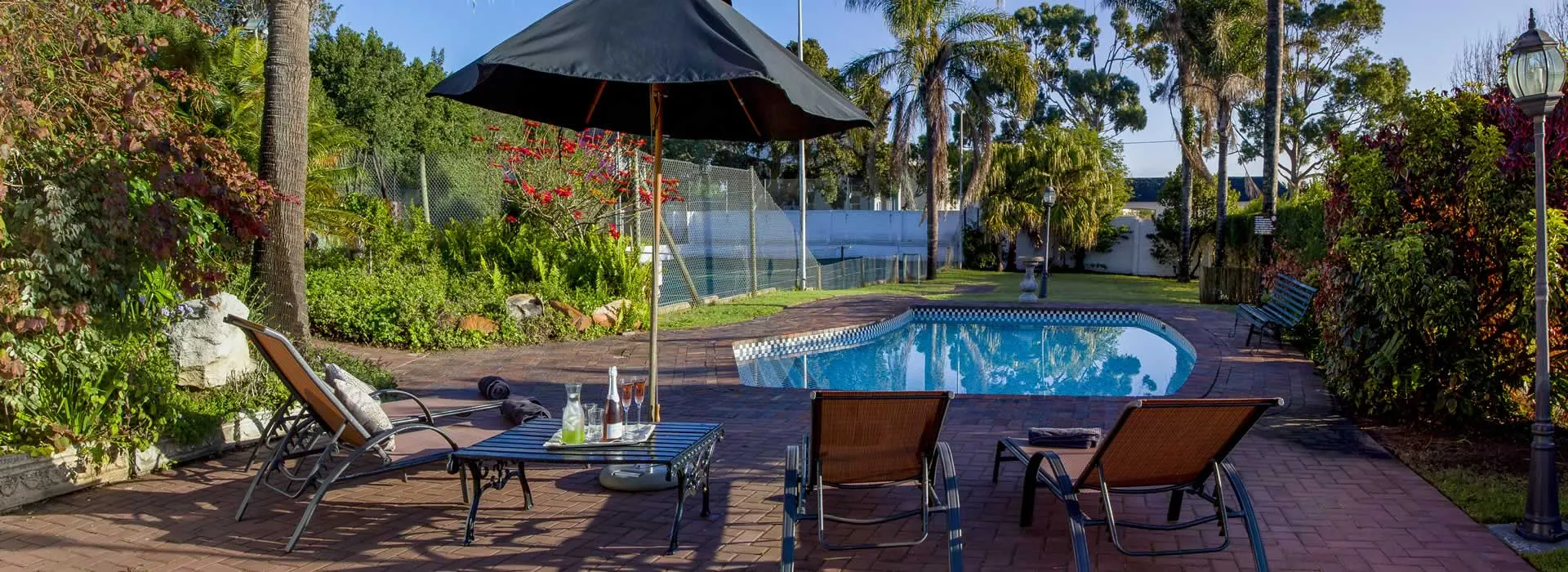Swimming pool with lounge chairs umbrella and surrounding greenery in a backyard