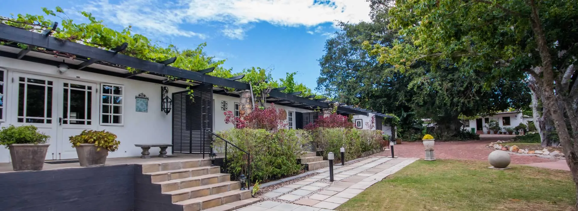 Row of quaint white cottages with greenery pathway and trees in a serene setting