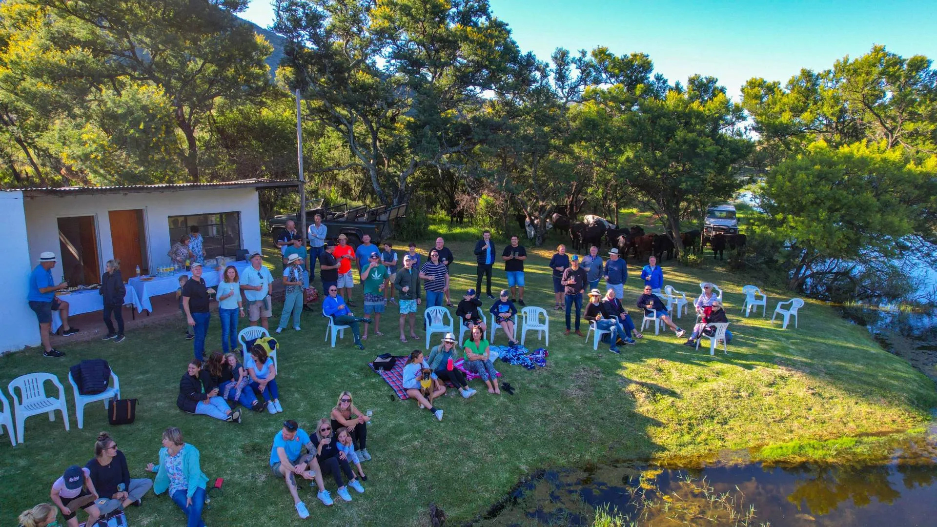 Group of people gathered outdoors near a lake some sitting some standing