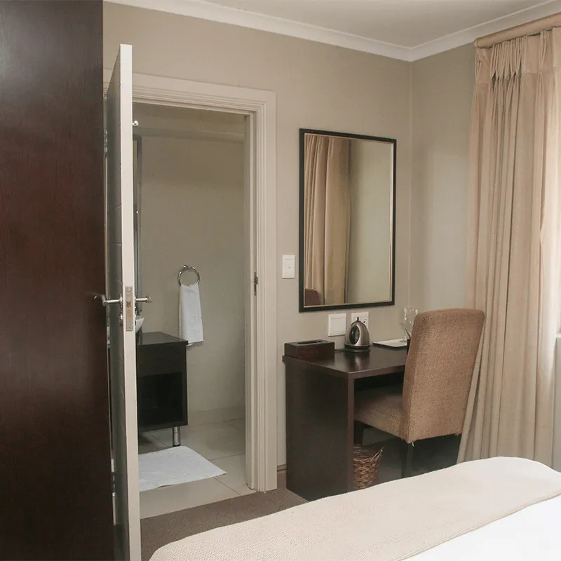 Hotel room with open door desk chair and bed with beige curtains
