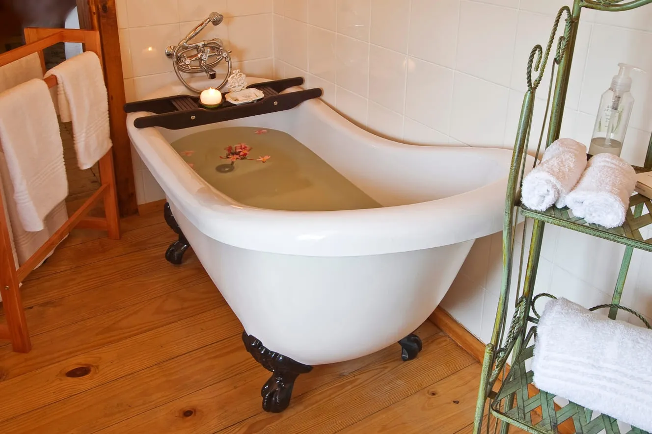 Vintage bathtub with green water wooden floor and towels on a metal rack