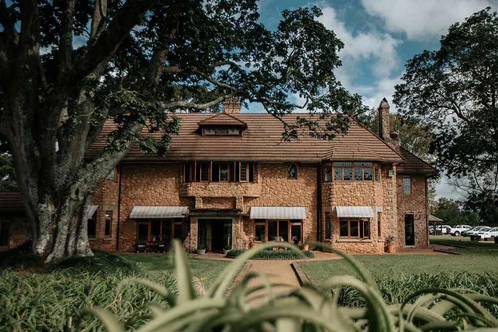 Large stone house with red roof surrounded by greenery and trees