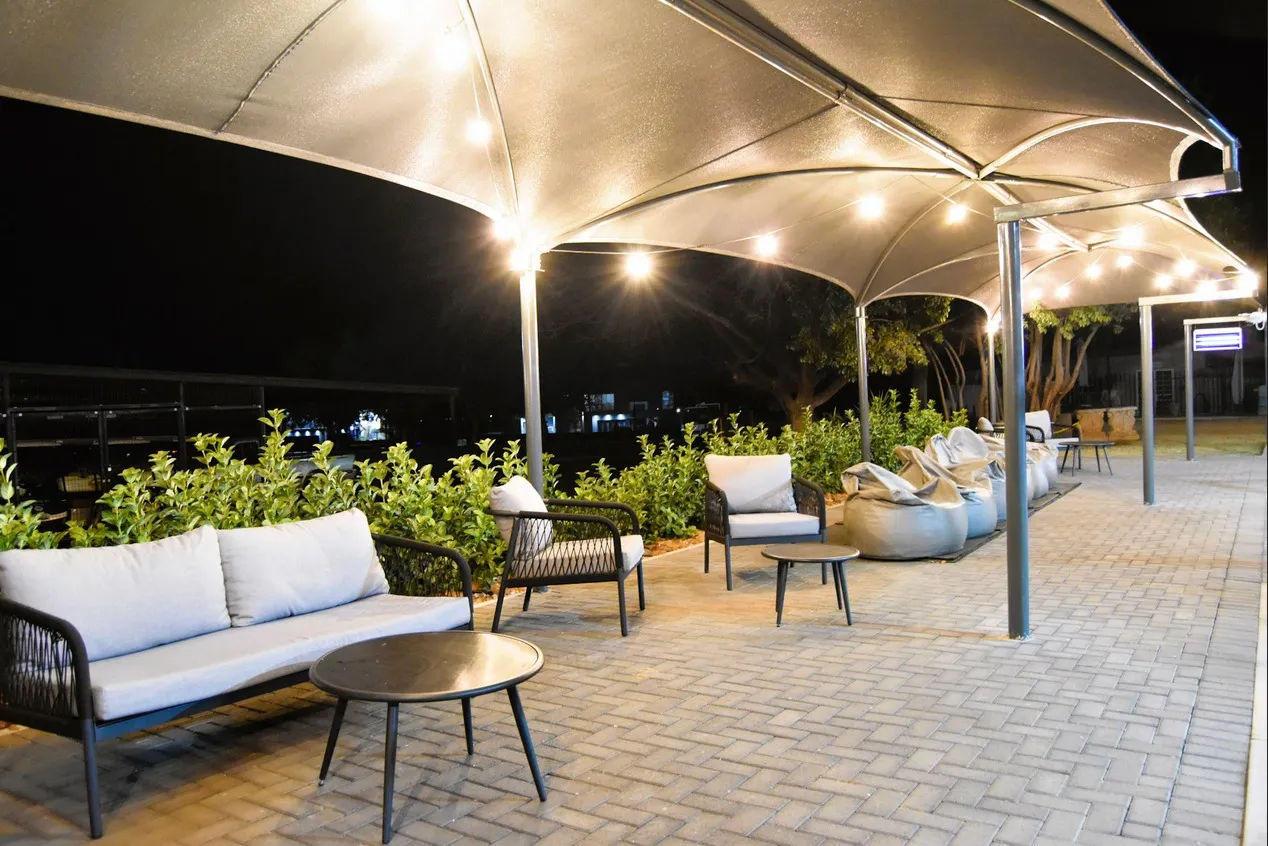 Outdoor seating area with sofas and chairs under illuminated canopies at night
