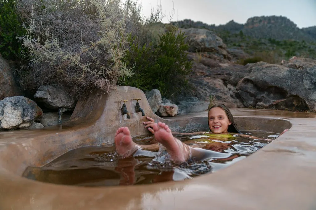 Child relaxing in a natural rock pool with feet up surrounded by desert landscape
