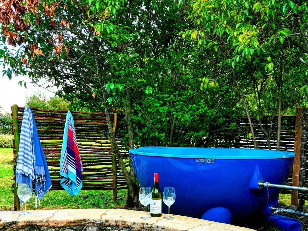 Blue hot tub in garden with wine bottle and glasses on stone table