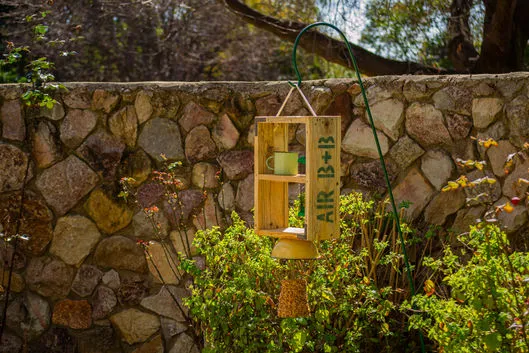 Wooden birdhouse on a post in front of a stone wall with greenery