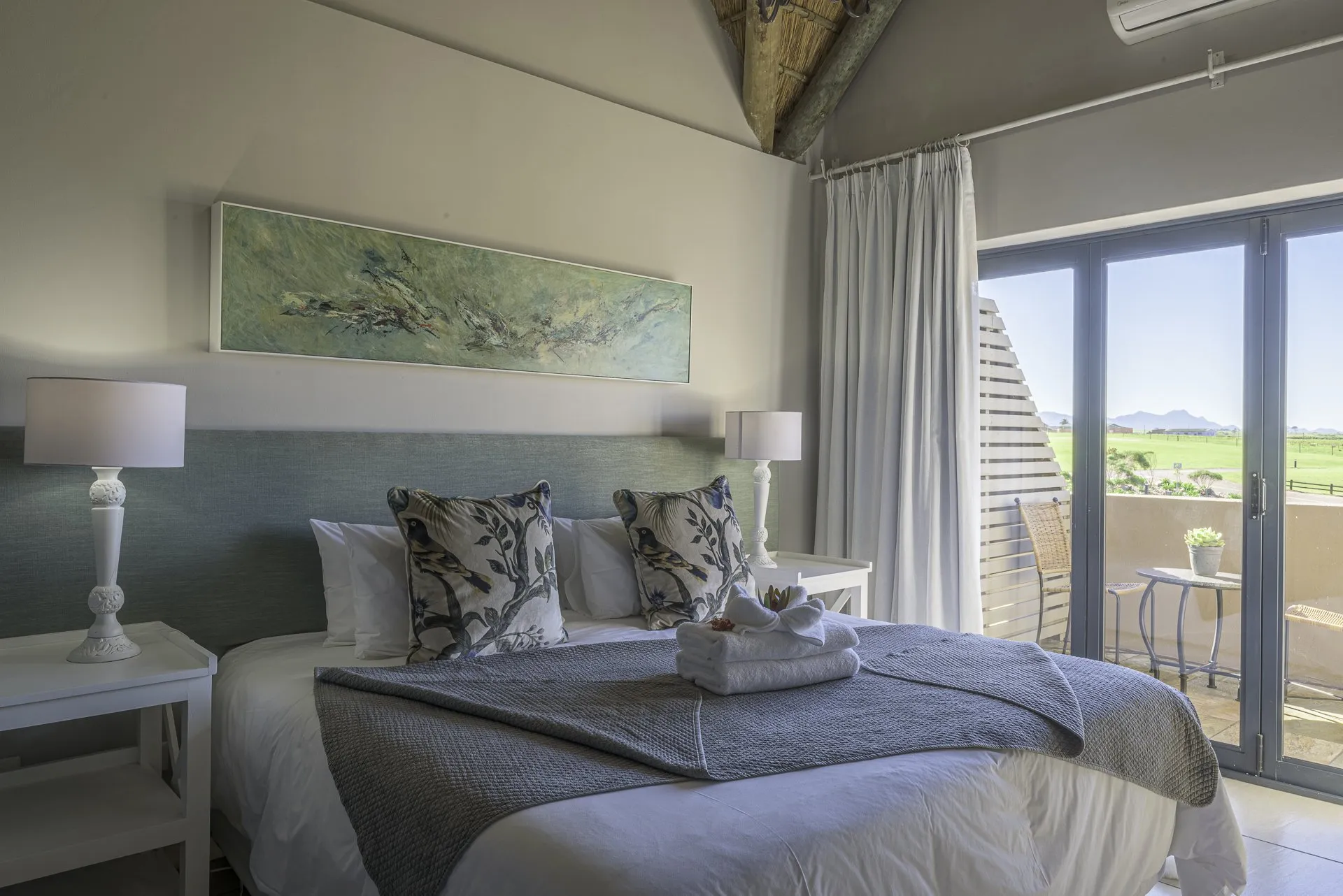 Modern bedroom with large bed pillows and view of outdoor patio through glass doors
