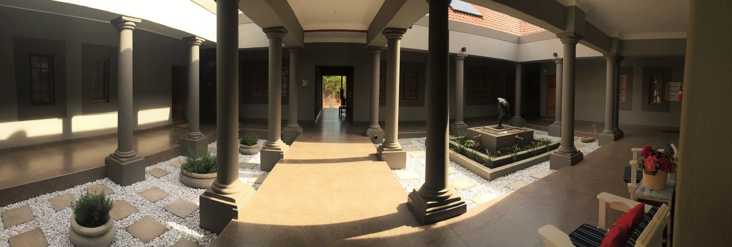 Courtyard with columns potted plants and a central pathway leading to an exit