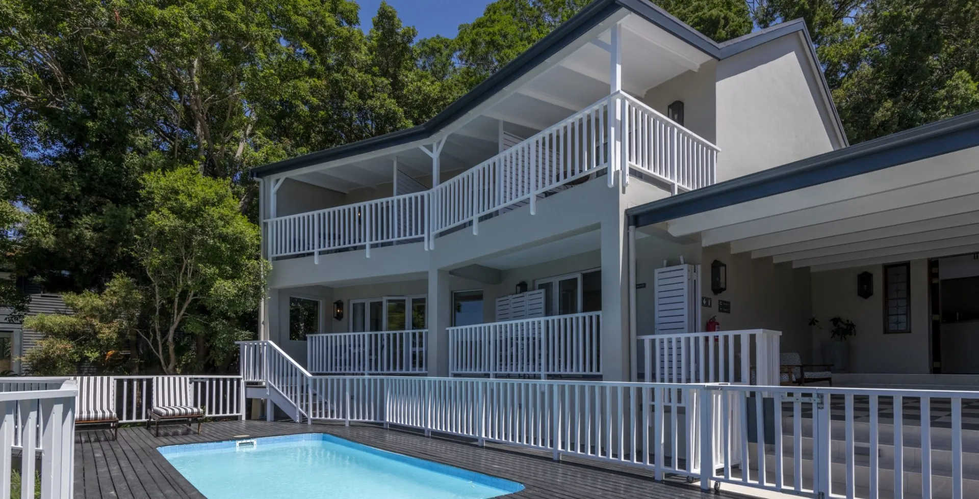 Twostory house with a swimming pool and white railings surrounded by trees