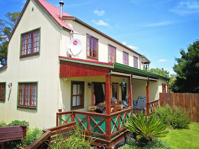 Twostory house with a veranda wooden fence and lush greenery in the background