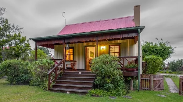 Small cottage with red roof wooden porch and lush greenery around