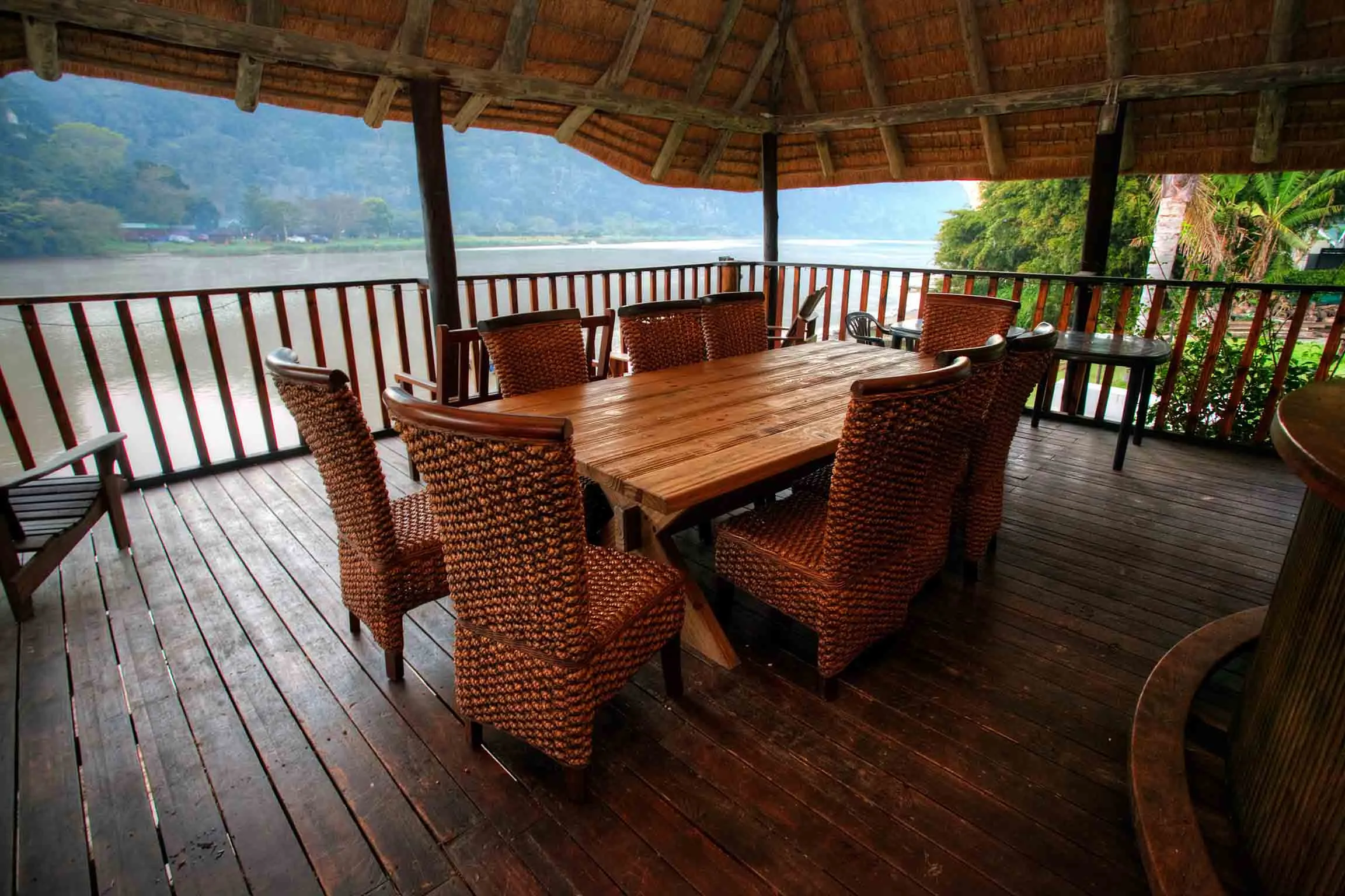 Wooden table with wicker chairs on a deck overlooking a river and mountains