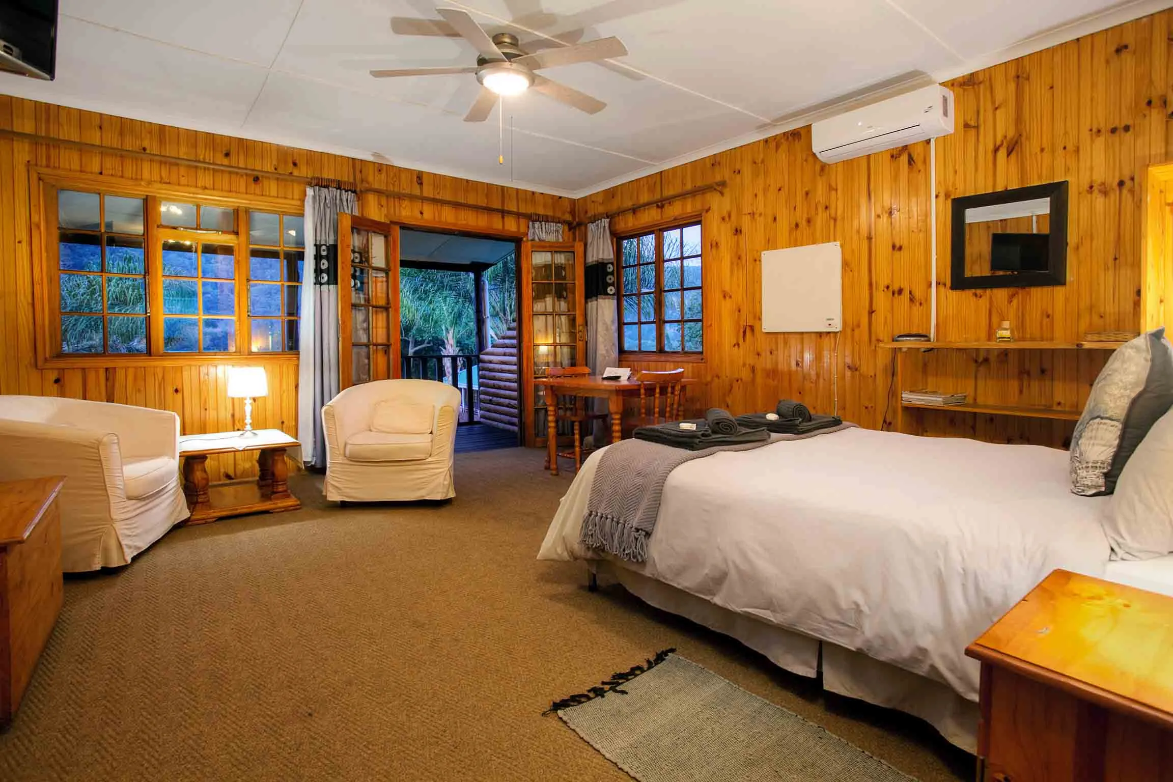 Cozy wooden bedroom with bed chairs and ceiling fan overlooking a balcony