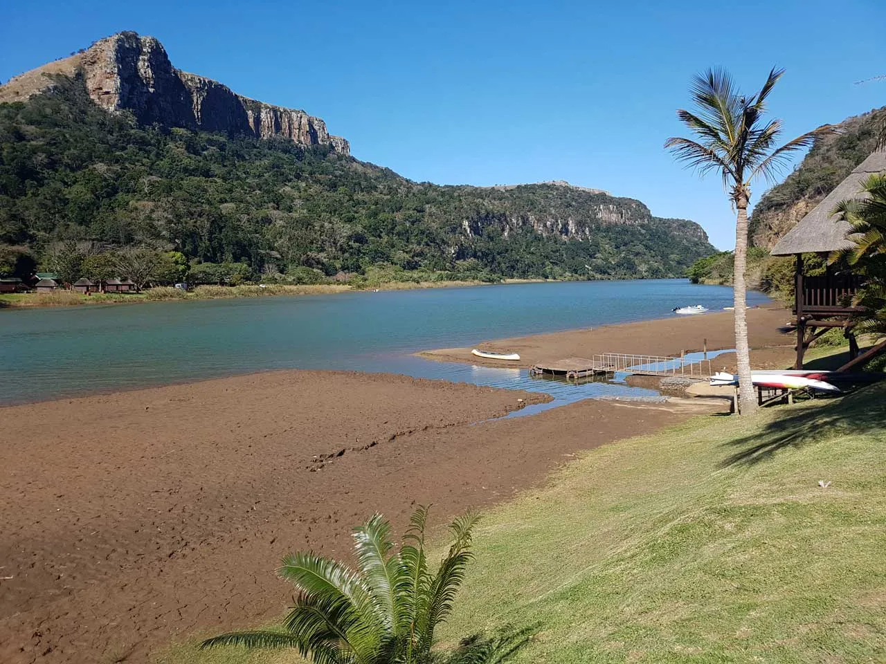 River with sandy shore palm tree and wooden dock in mountainous landscape