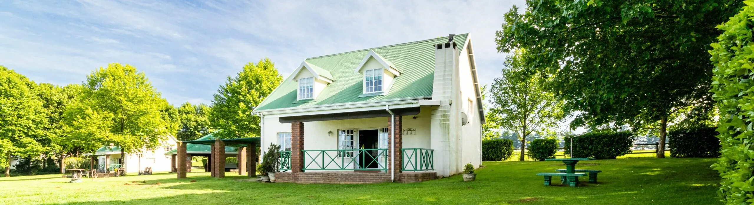 Cottage with green roof in a lush garden with trees and picnic table
