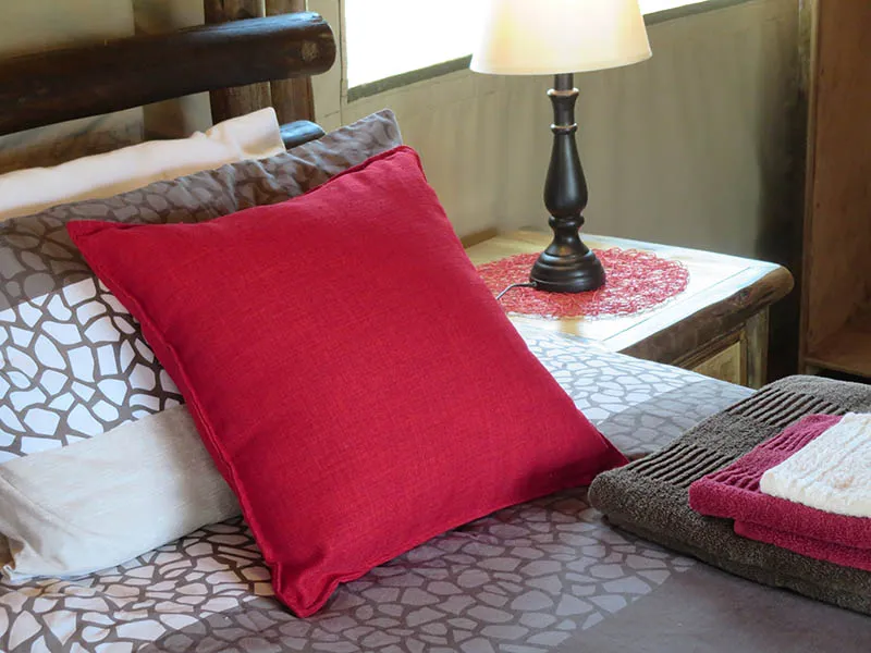 Red pillow on a bed with patterned bedding and a bedside lamp
