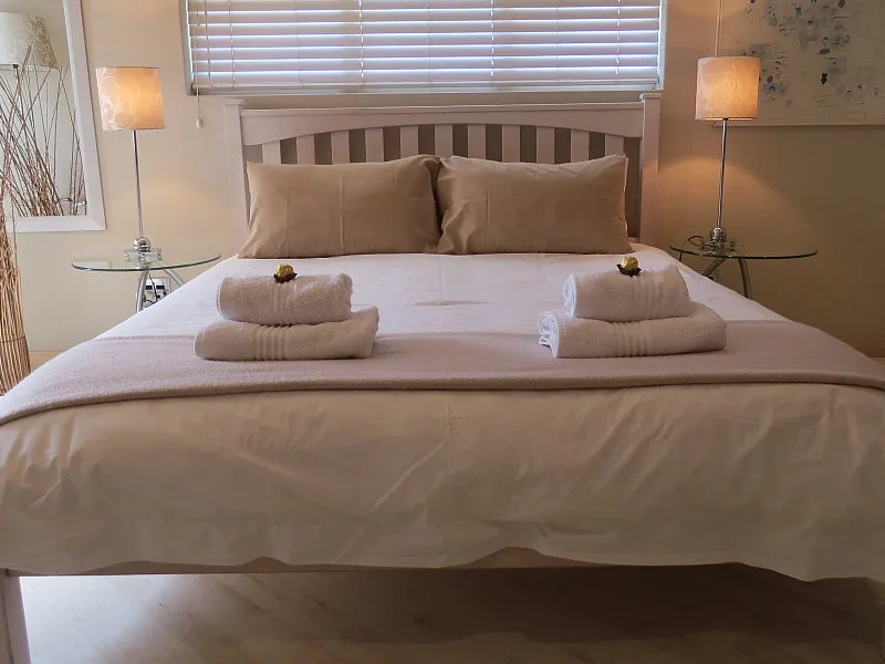 Neatly made bed with towels lamps and window blinds in a bedroom