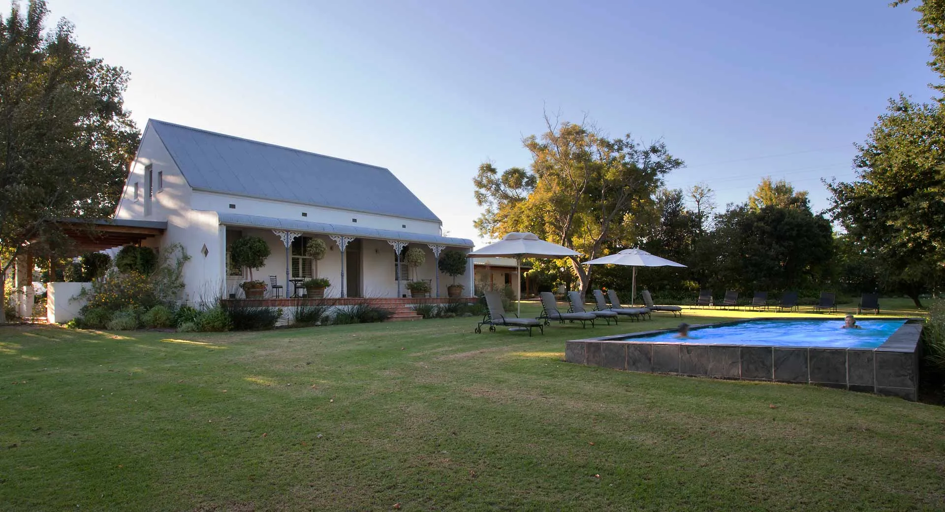 White house with grey roof green lawn and swimming pool in a garden