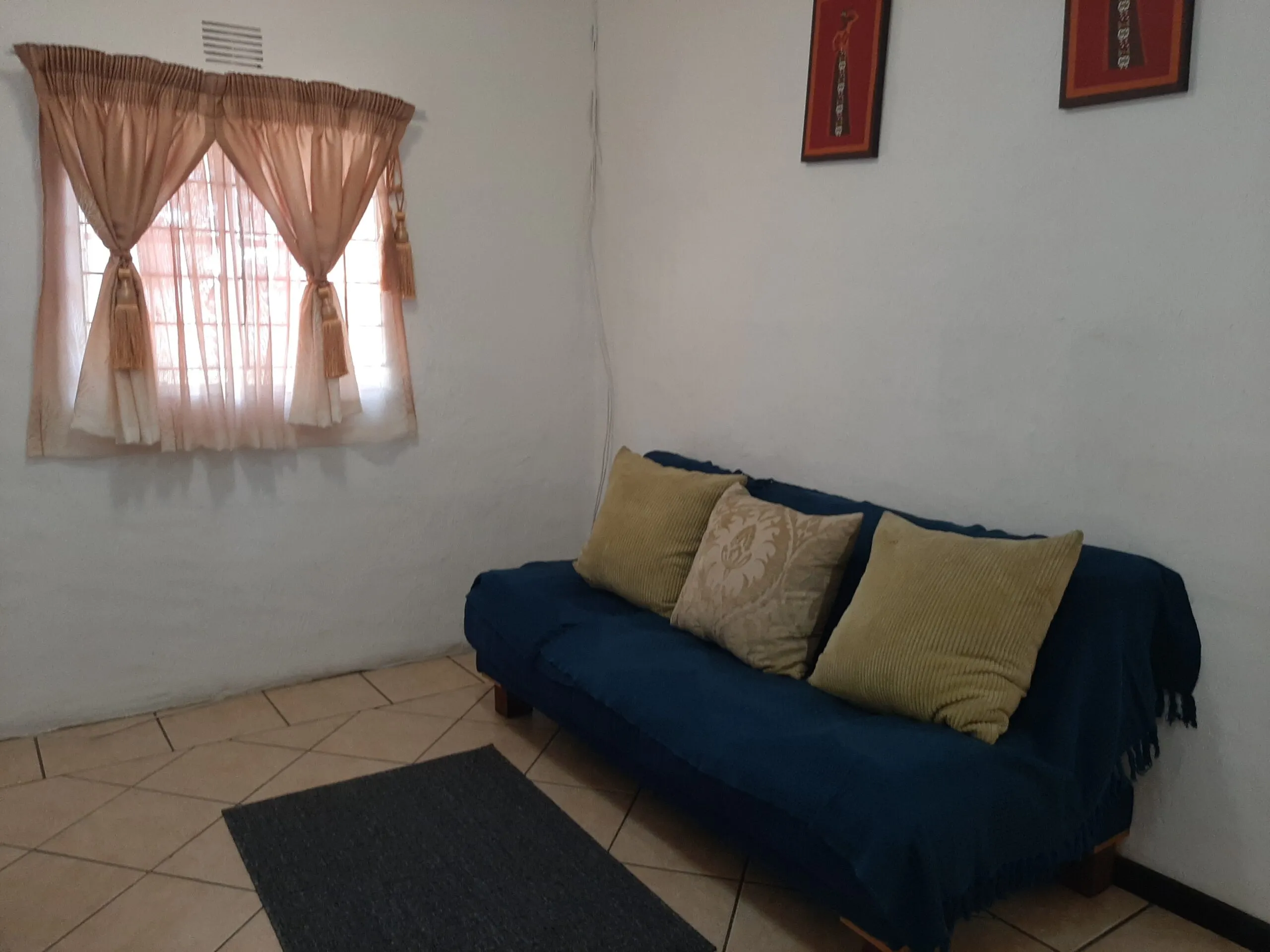 Blue sofa with three pillows in a whitewalled room with a window