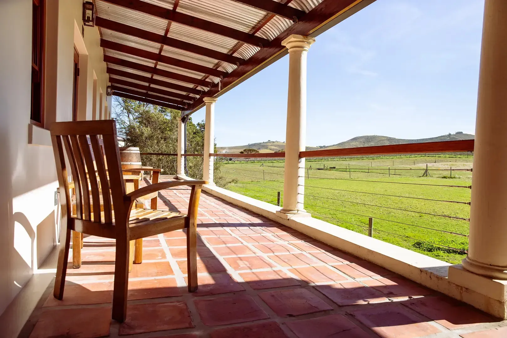 Wooden chair on a tiled veranda overlooking a green field with hills in the distance