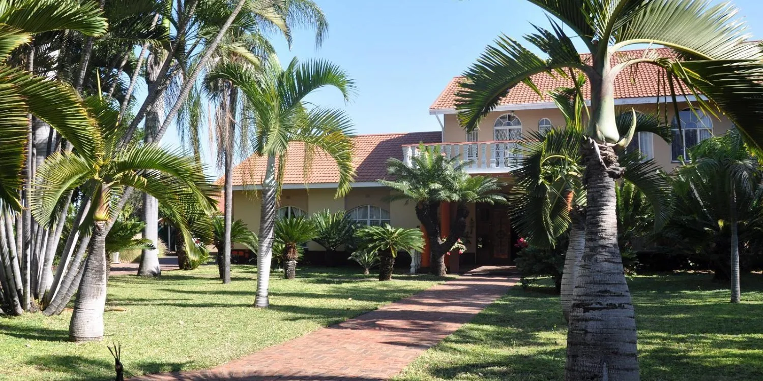 Large house with redtiled roof surrounded by palm trees and a brick pathway