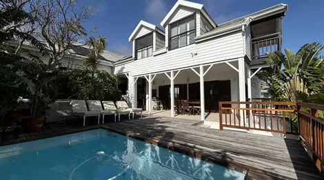 White house with wooden deck pool and outdoor seating in a tropical setting