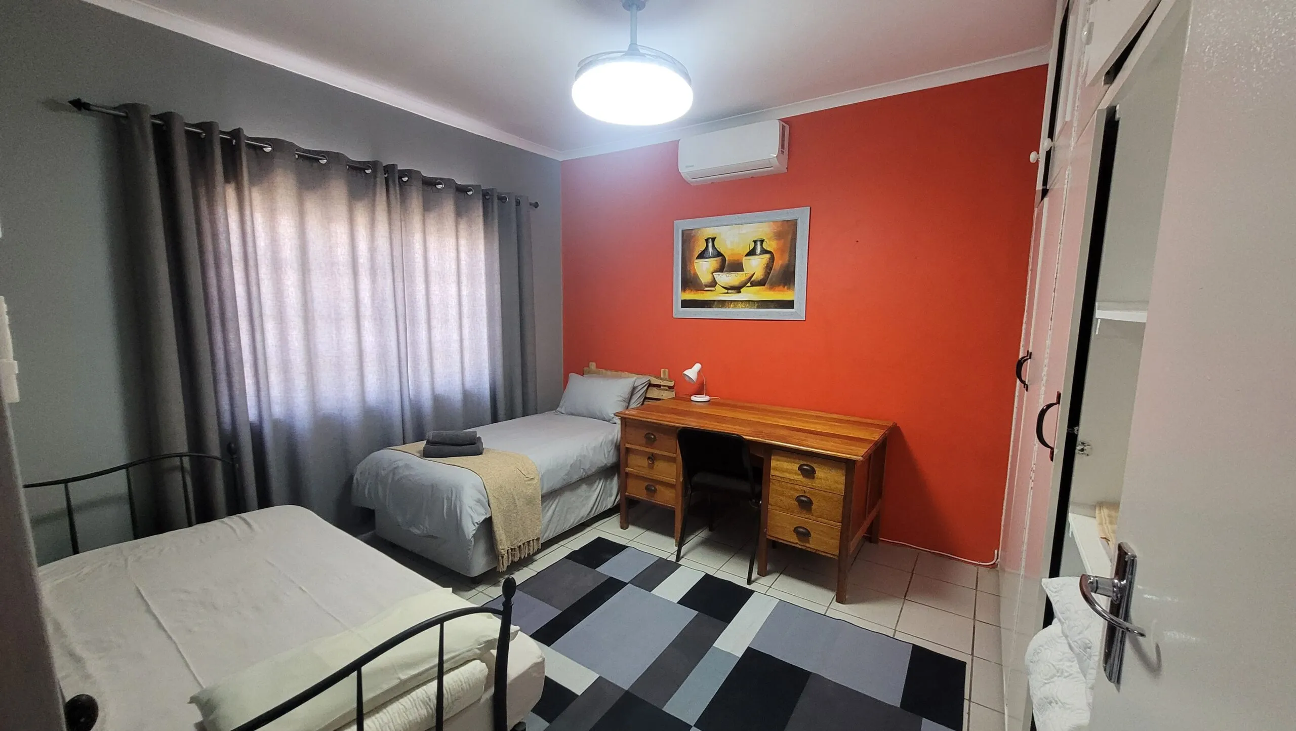 Bedroom with two single beds desk and red accent wall with artwork