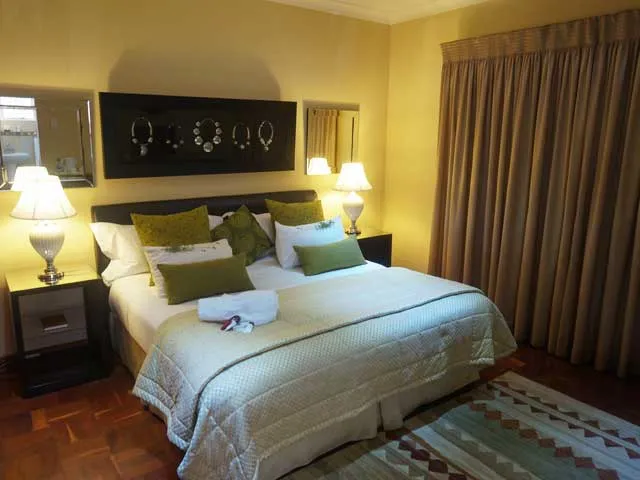 Bedroom with a large bed yellow walls and brown curtains on wooden floor