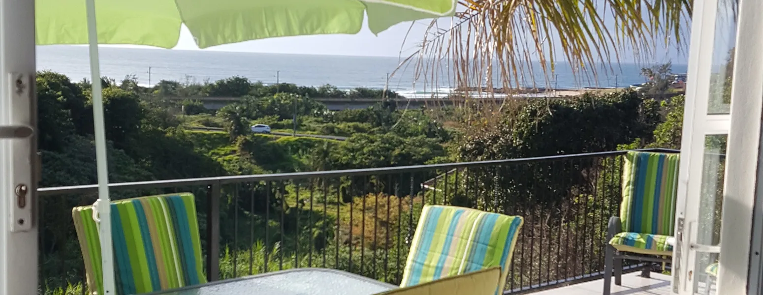 Balcony with green chairs table and ocean view under a green umbrella