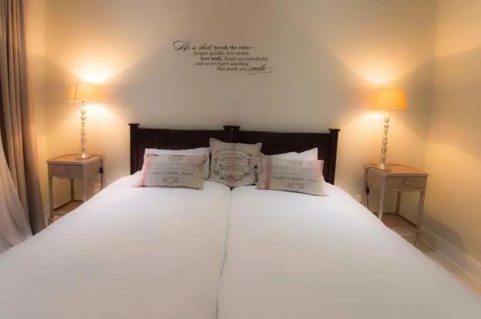 Bedroom with two twin beds pillows lamps and wall quote
