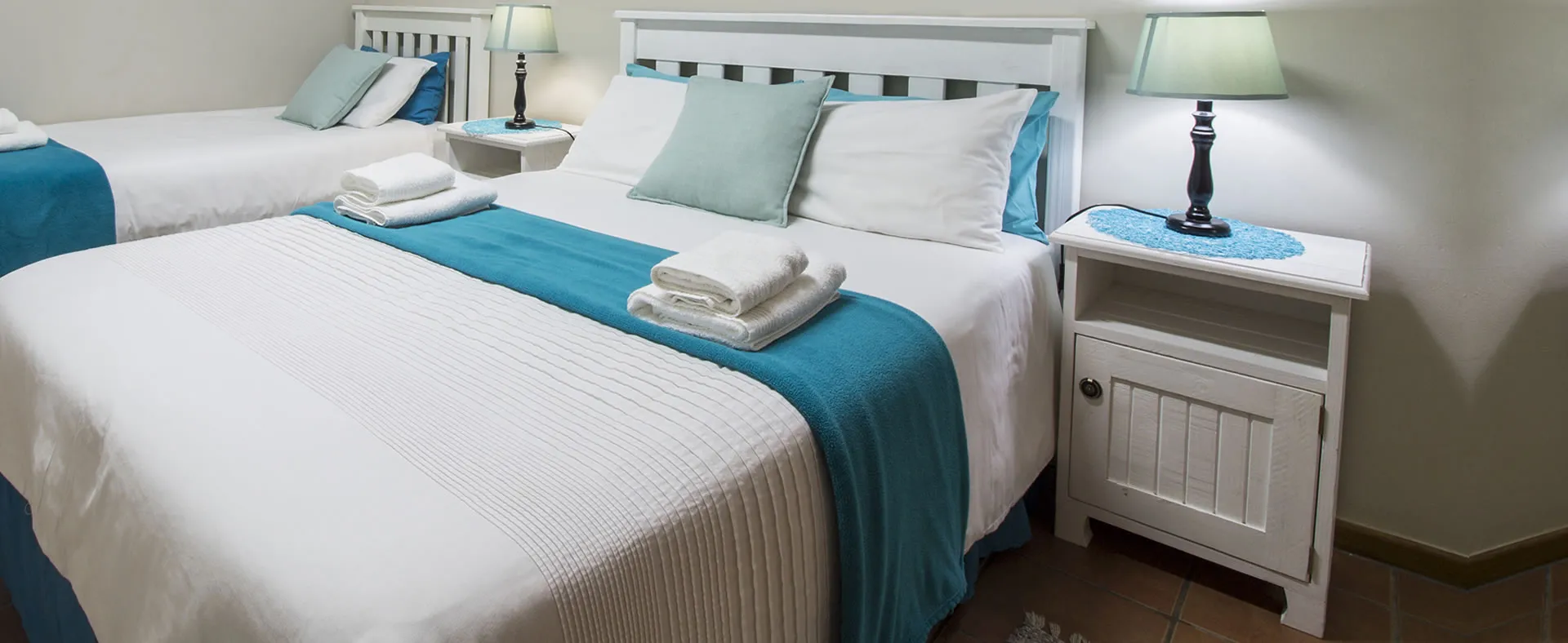 Two neatly made beds in a bedroom with bedside tables and lamps