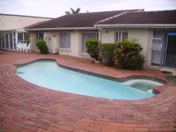 Swimming pool with brick patio and singlestory house in the background