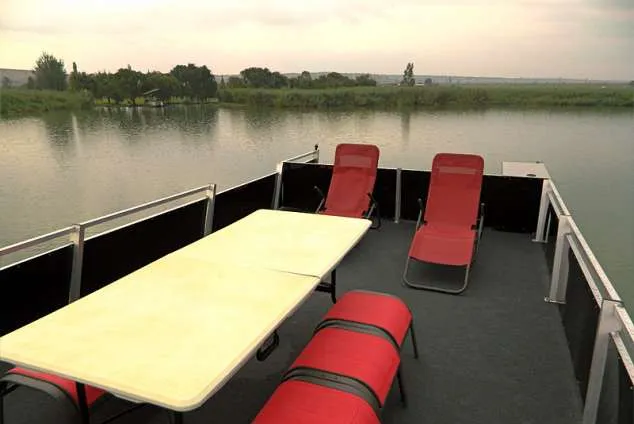 A boat deck with table chairs and red lounge chairs overlooking a lake
