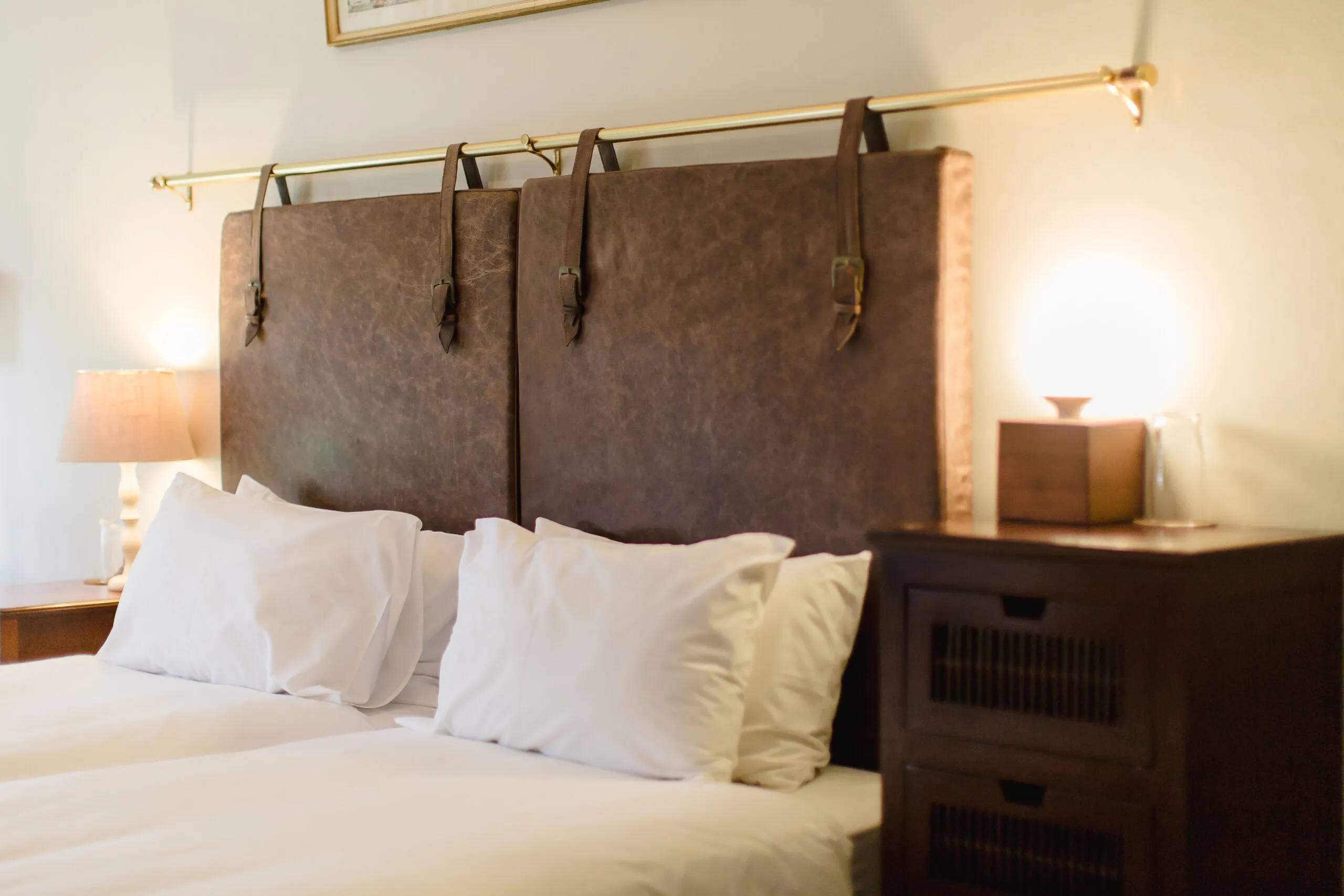 A bed with brown leather headboard white pillows and bedside table with lamp