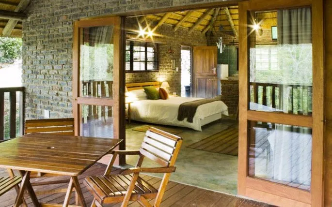 Wooden deck with table and chairs overlooking a cozy bedroom with a bed